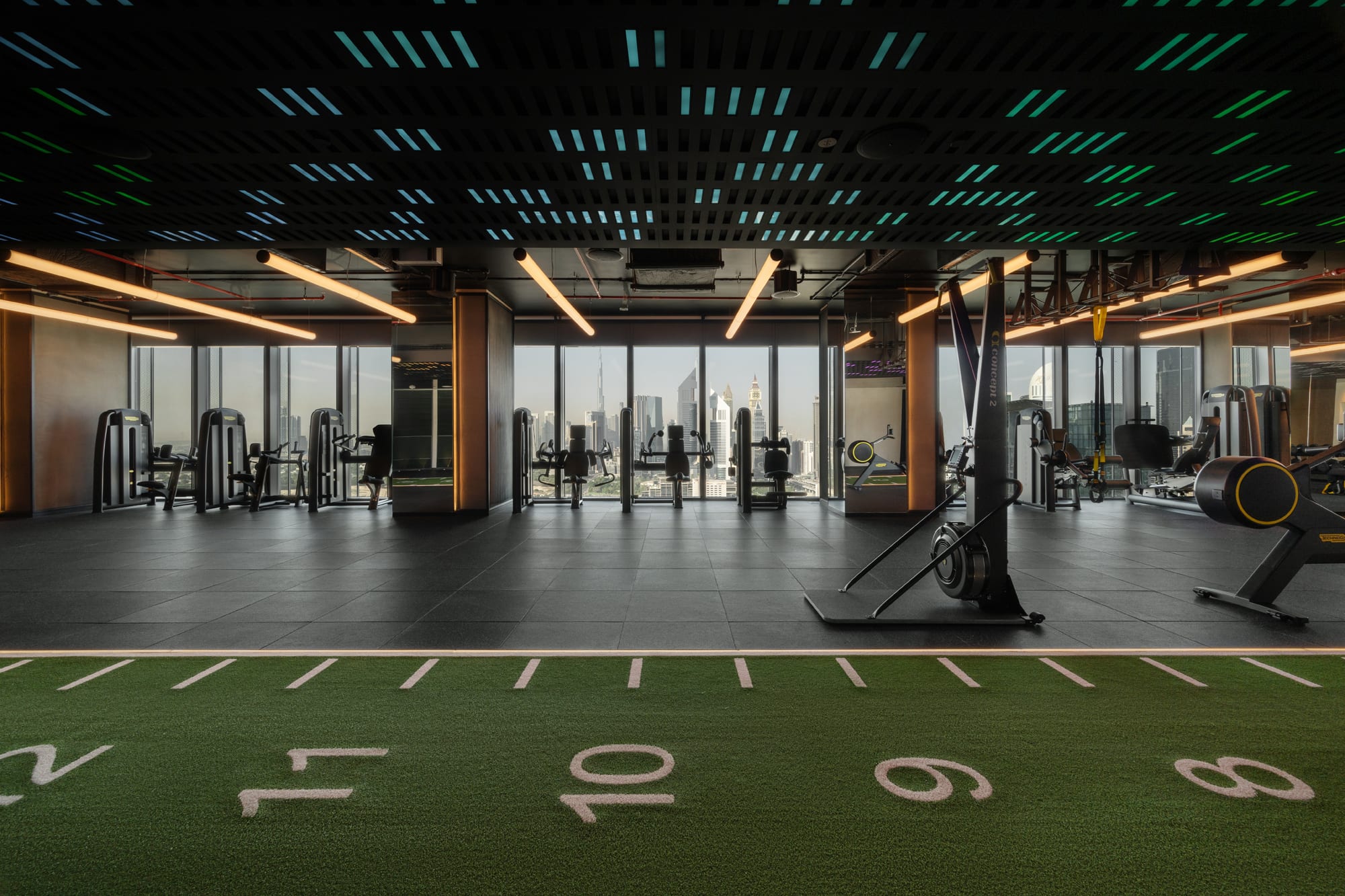 Siro One Zabeel, Siro Hotels Modern gym interior with cardio equipment, green turf flooring, and city skyline view through floor-to-ceiling windows