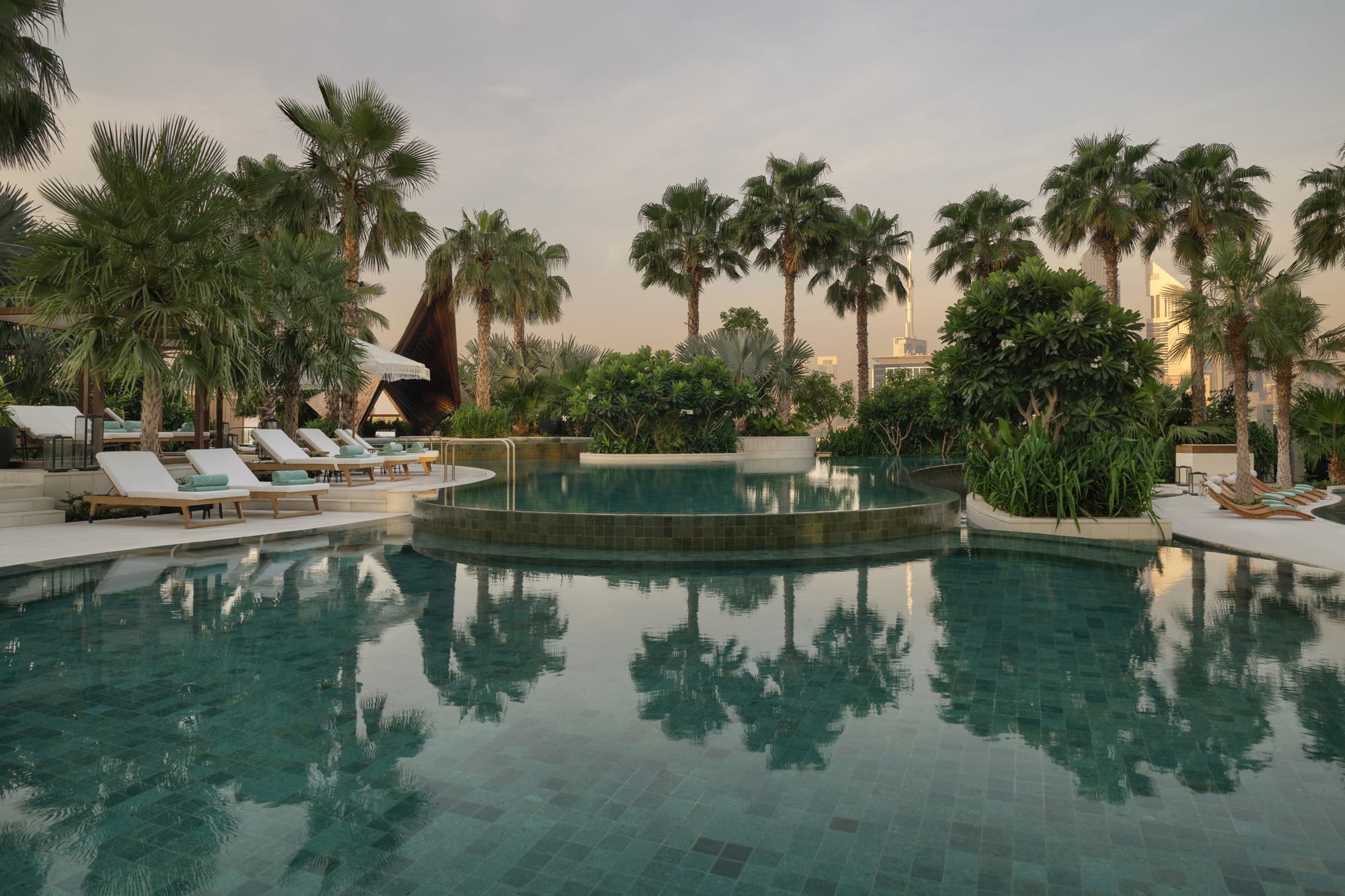 Luxury resort pool with palm trees, loungers, and tropical landscape at sunset
