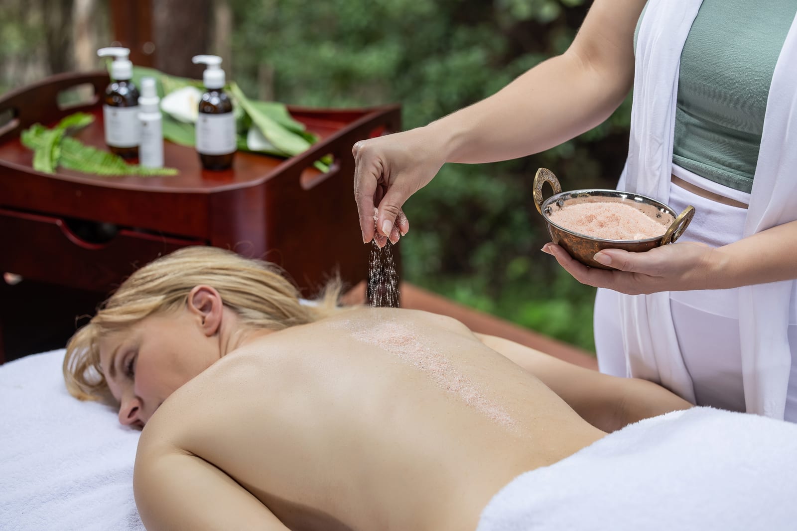 Spa Treatment with Salt Scrub A spa therapist applying a salt scrub treatment to a client during an outdoor wellness session, with massage oils and natural ingredients visible.