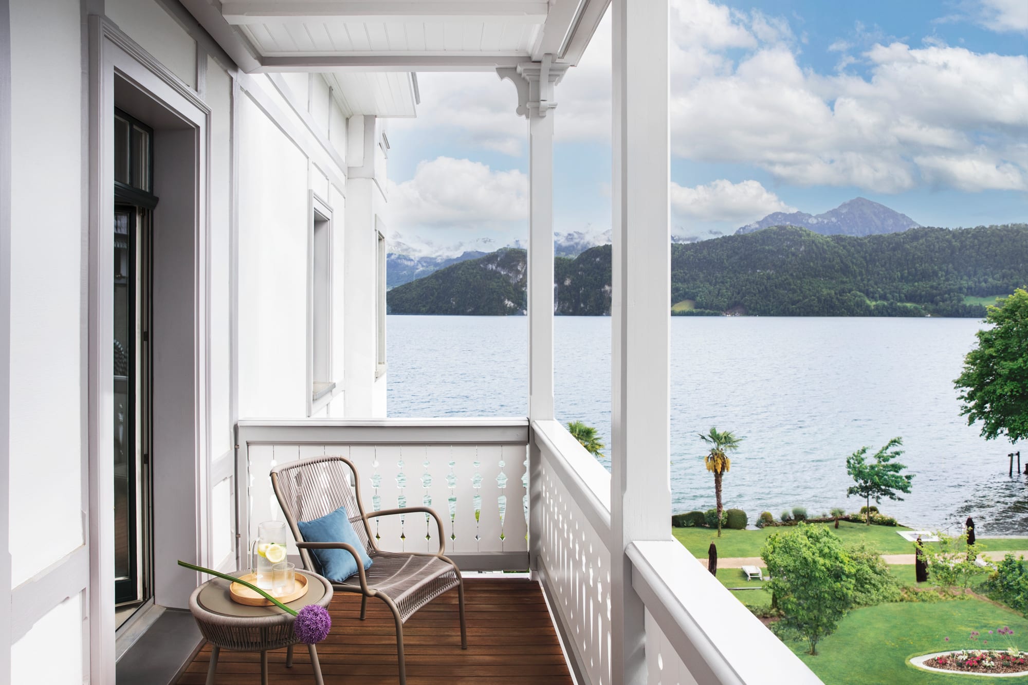Superior Room (1) White lakeside balcony with wicker chair overlooking mountain lake and forested shores