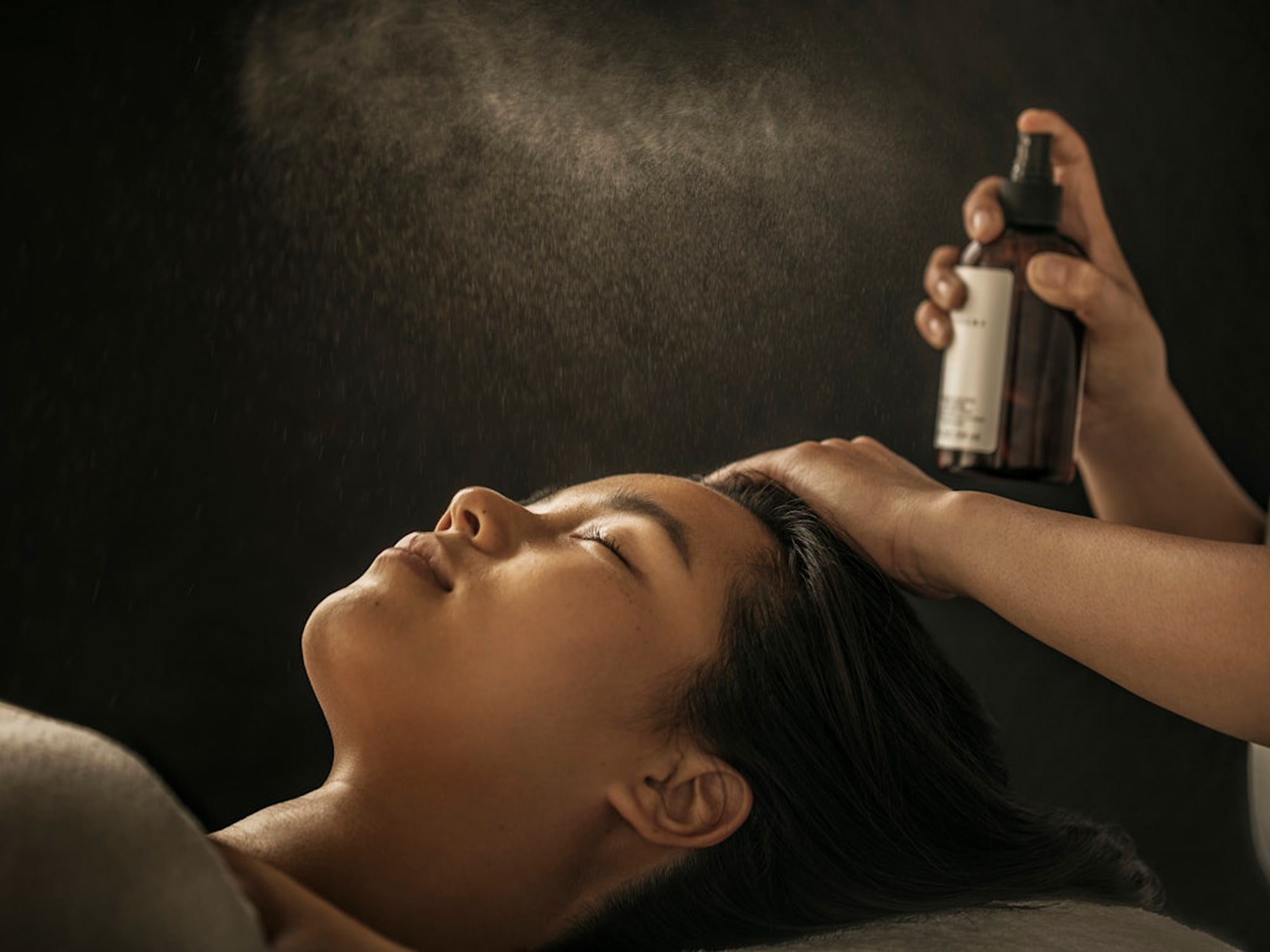 Woman receiving hair treatment spray applied to her head during salon service