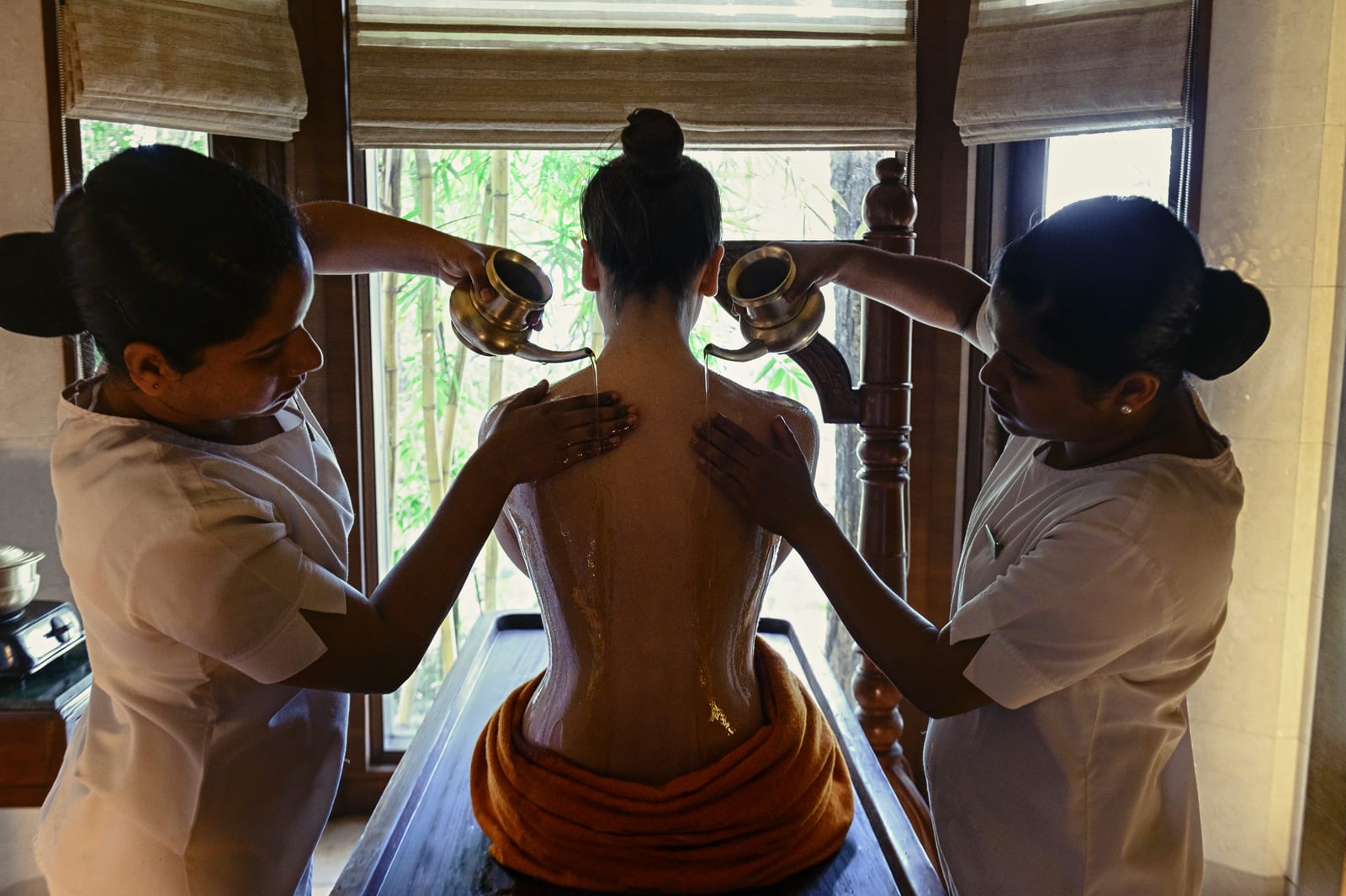 Wellness_Ayurveda_therapy 2 Two therapists pouring warm oil on man's back during traditional Ayurvedic massage therapy treatment
