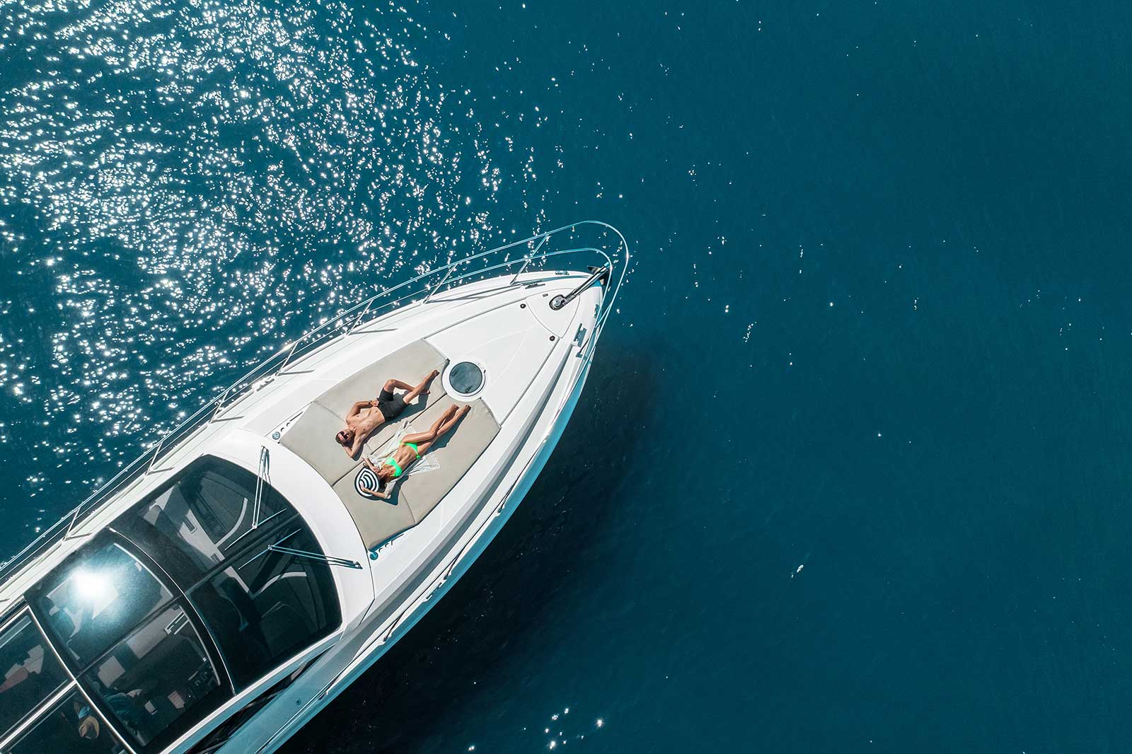 Aerial view of white speedboat with two people sunbathing on deck in turquoise water