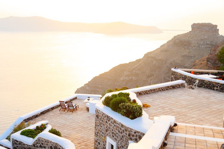 Whitewashed terrace with potted plants overlooking golden-hour sea and volcanic cliffs
