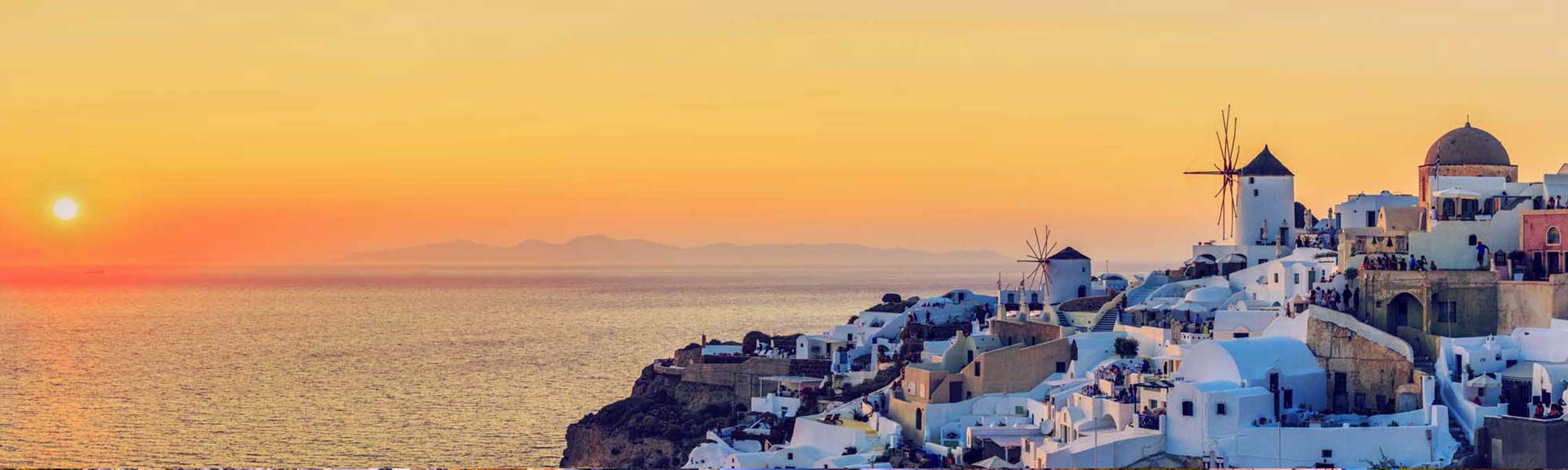 Santorini sunset with whitewashed buildings, windmills, and red-domed church overlooking Aegean Sea