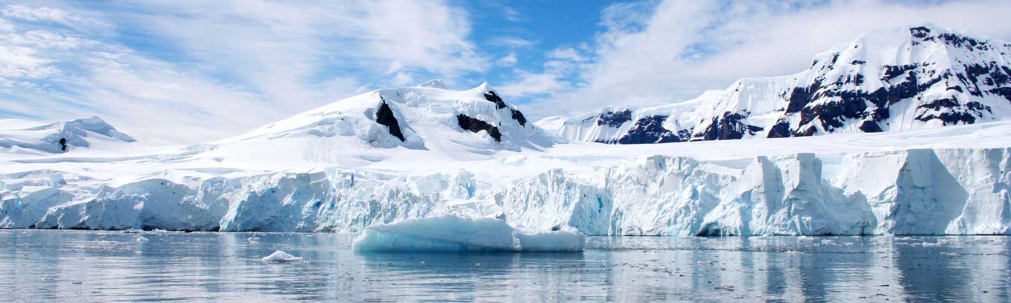 Antarctic landscape with glacier cliffs, icebergs, and snow-covered mountains under blue sky