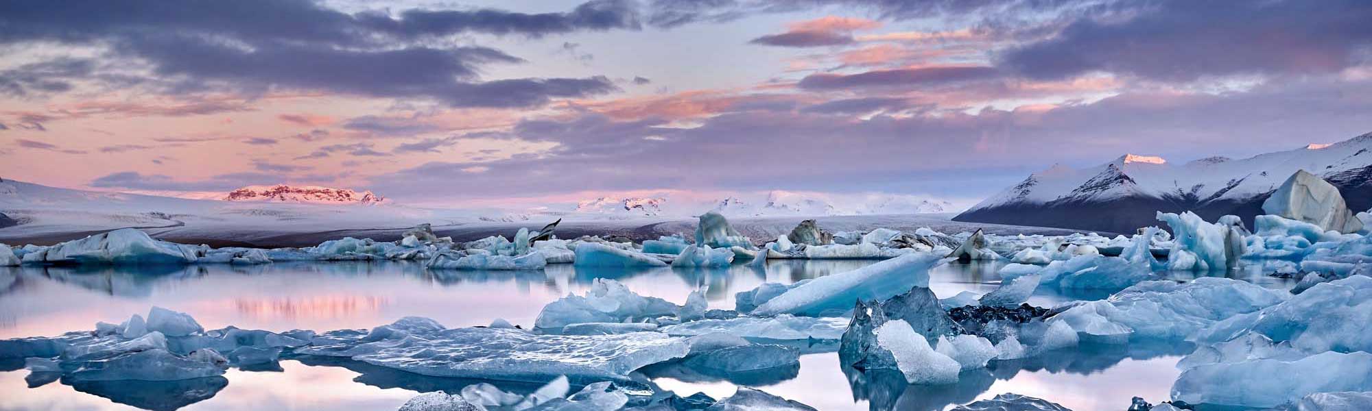 Glacier lagoon at sunset with blue icebergs floating in calm water and snow-capped mountains