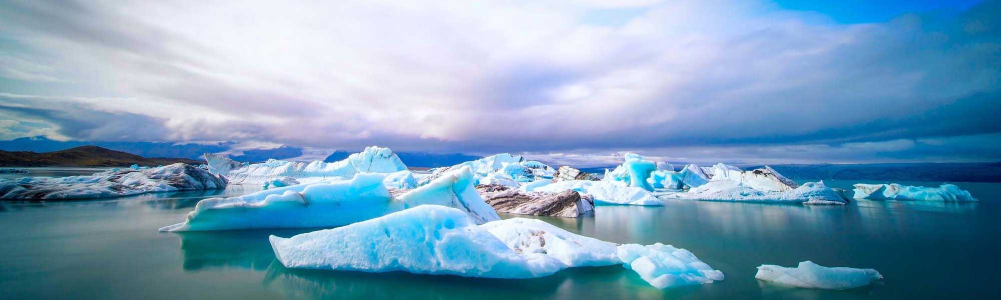 Icebergs floating in turquoise glacial lake at dusk with mountains in background
