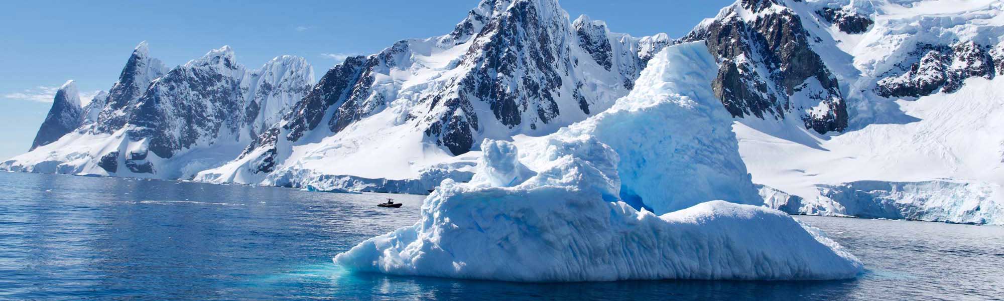 Snow-covered Antarctic mountains and icebergs floating in deep blue water under clear sky