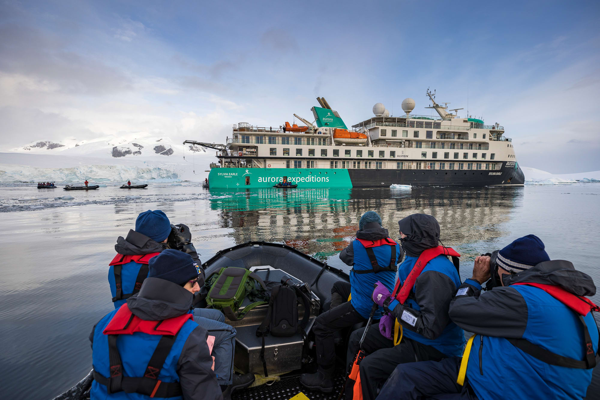 A group of travelers in blue and red waterproof gear ride a Zodiac boat near the Aurora Expeditions