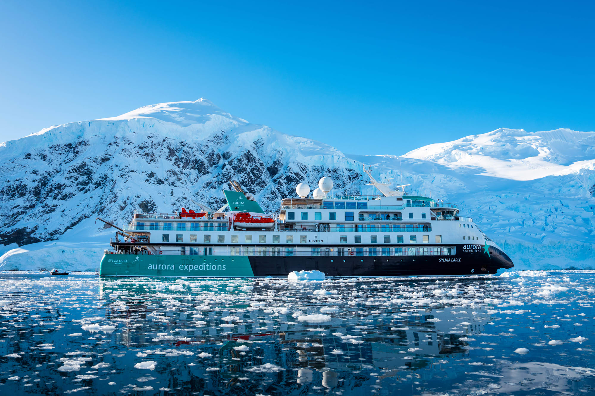 An expedition cruise ship navigating through icy waters with snow-capped mountains and glaciers