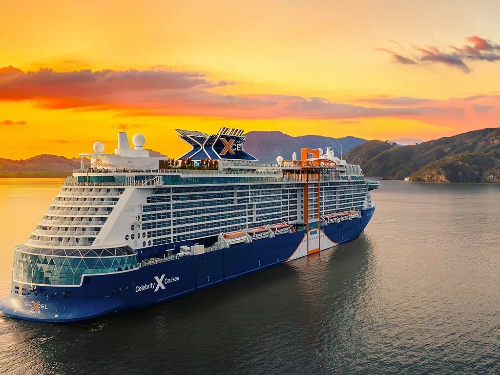 A large Celebrity Cruises ship anchored in calm waters with a dramatic golden sunset