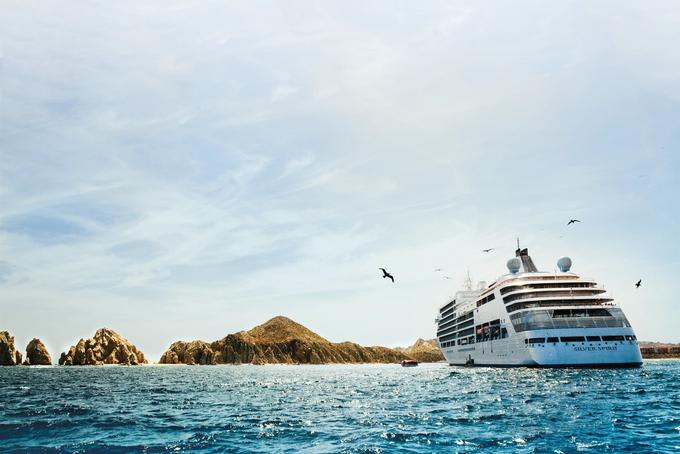 A pristine white cruise ship anchored near rugged rocky islands with turquoise blue waters and