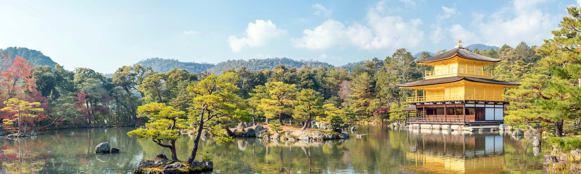 A serene landscape featuring the iconic gold-leaf covered Kinkaku-ji (Golden Pavilion) set against a tranquil pond with pine trees and mountains in the background. The pavilion reflects perfectly in the still water, creating a mesmerizing scene of Japanese architectural beauty.