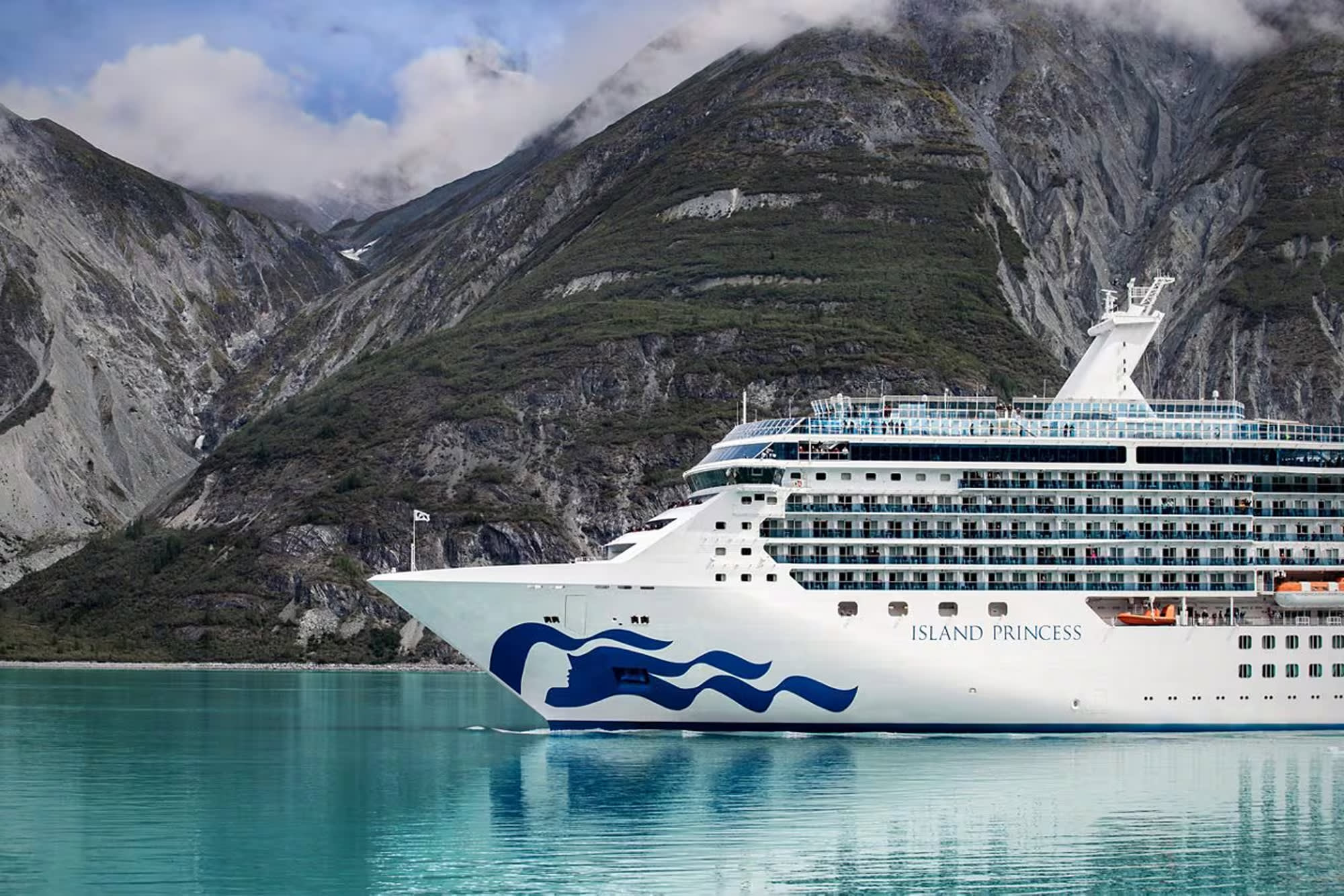 A white Princess Cruises ship sailing through turquoise waters with dramatic rocky mountain