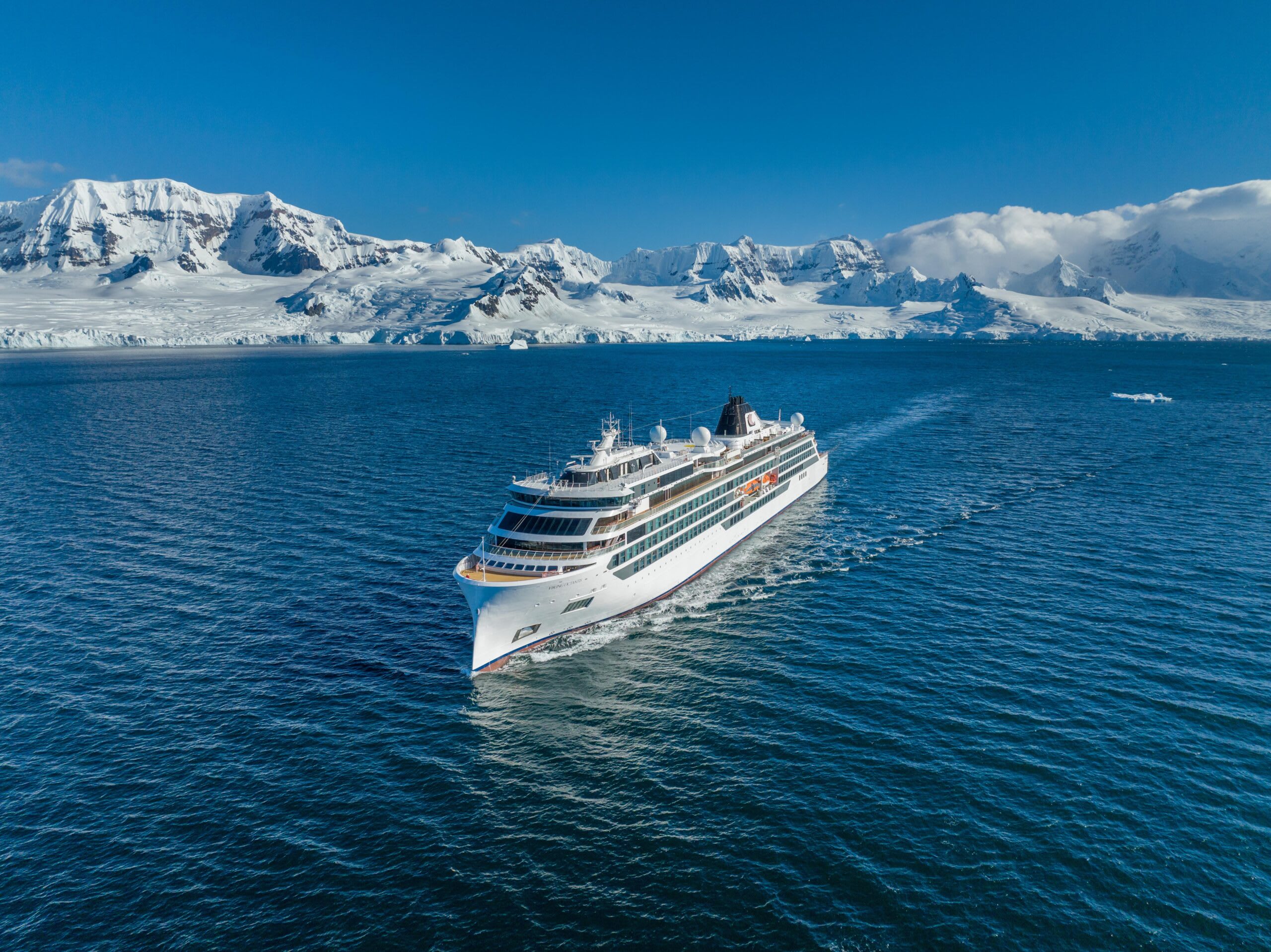 A white cruise ship sailing through deep blue waters with a dramatic snow-covered mountain