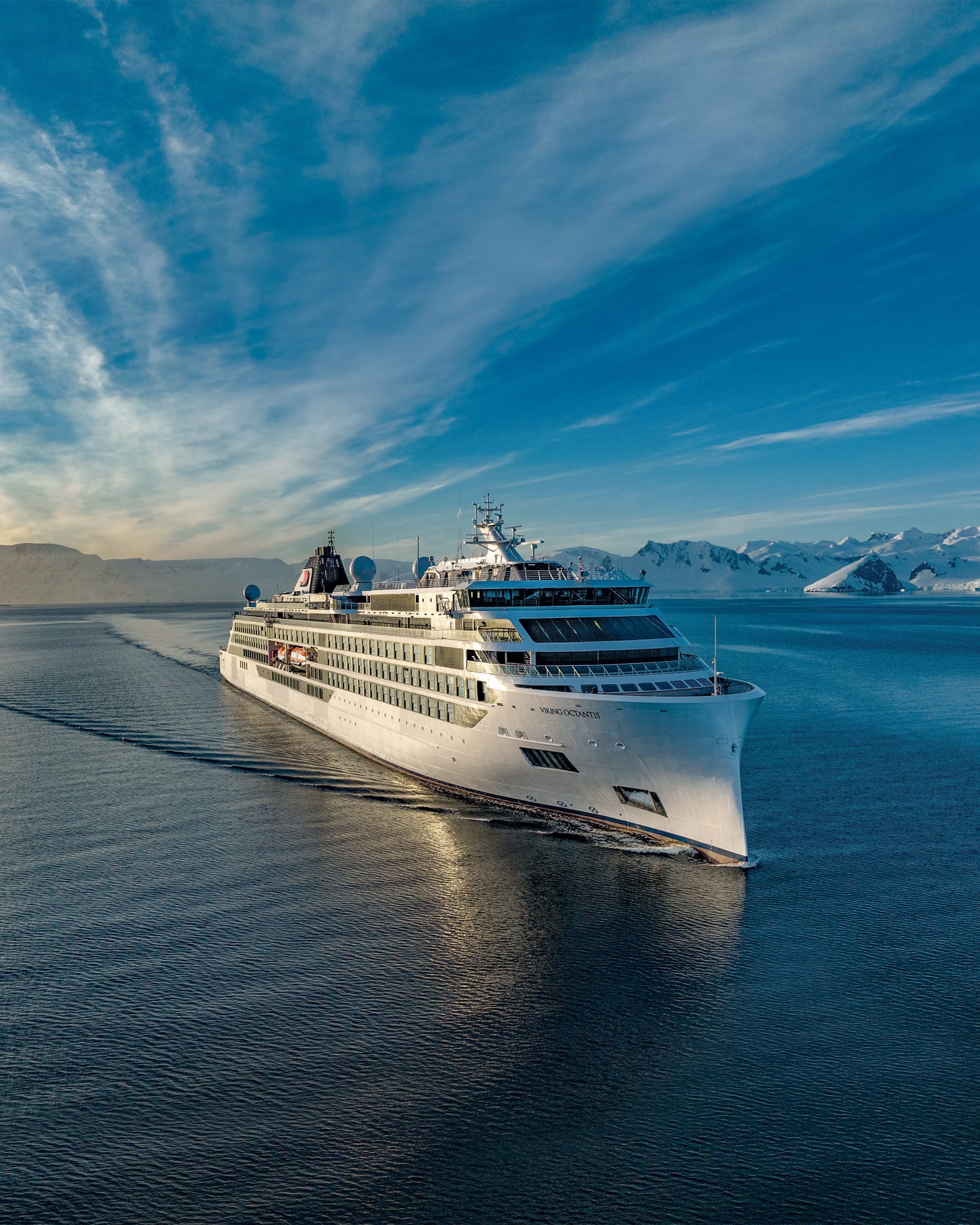 A pristine white cruise ship sailing through calm blue waters with snow-capped mountains
