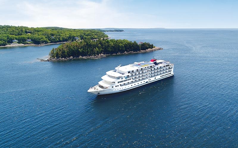 Luxury Cruise Ship in Coastal Landscape A white cruise ship sailing near a forested coastline with rocky shores and green islands