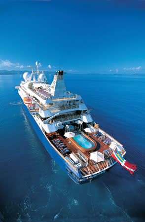 An aerial view of a pristine white cruise ship sailing on crystal blue waters, featuring multiple