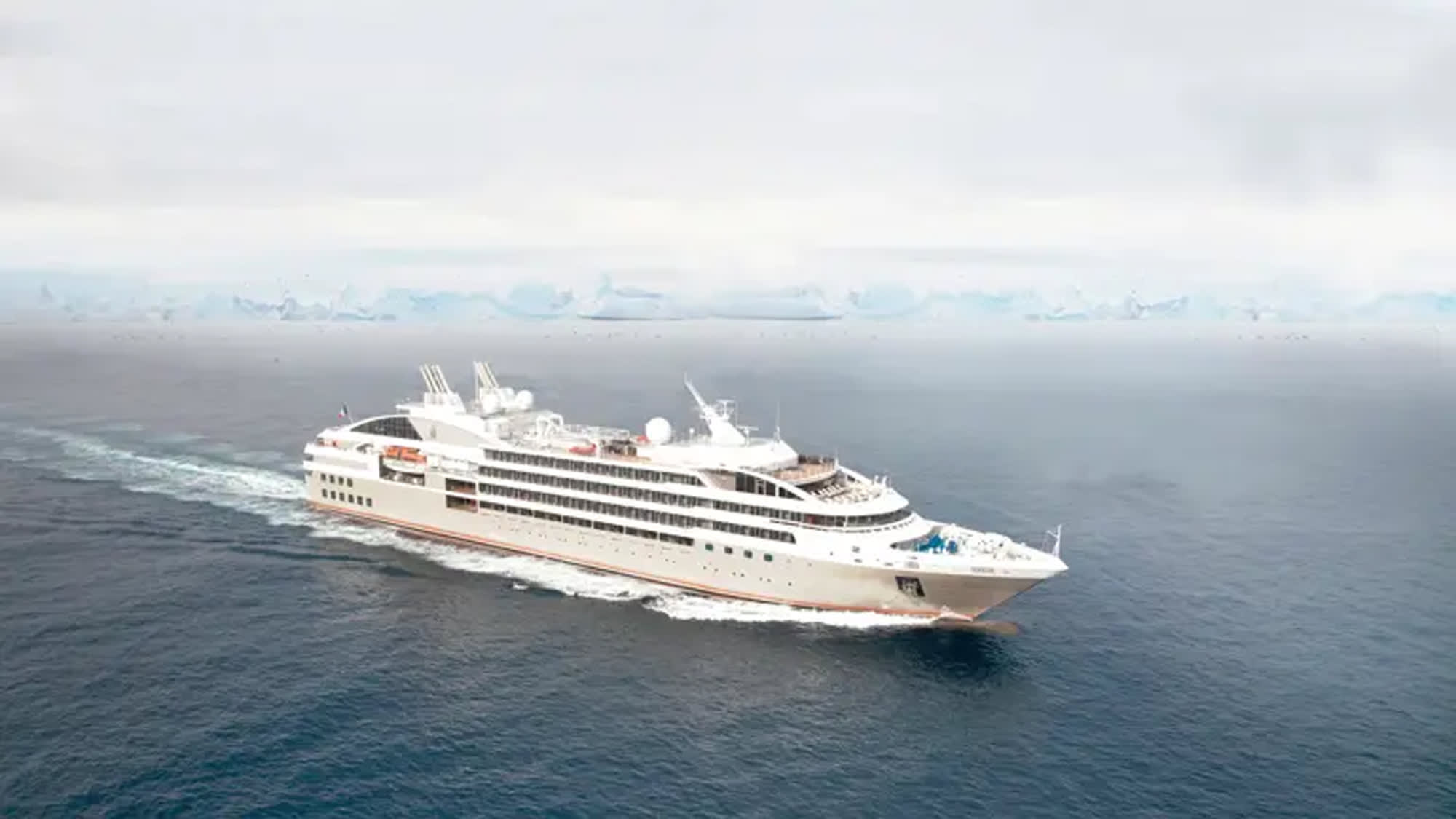 A sleek white expedition cruise ship navigating through cold, misty waters with an icy horizon