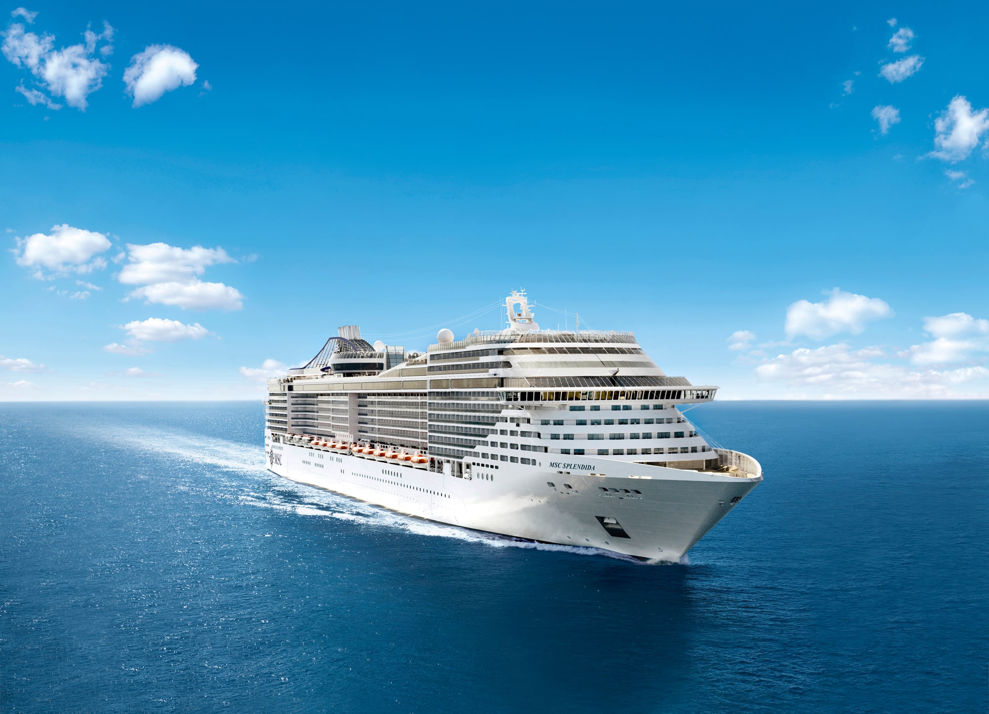 MSC Splendida Cruising Bright Blue Waters A large white MSC cruise ship sailing on a vibrant blue ocean under a clear sky with scattered