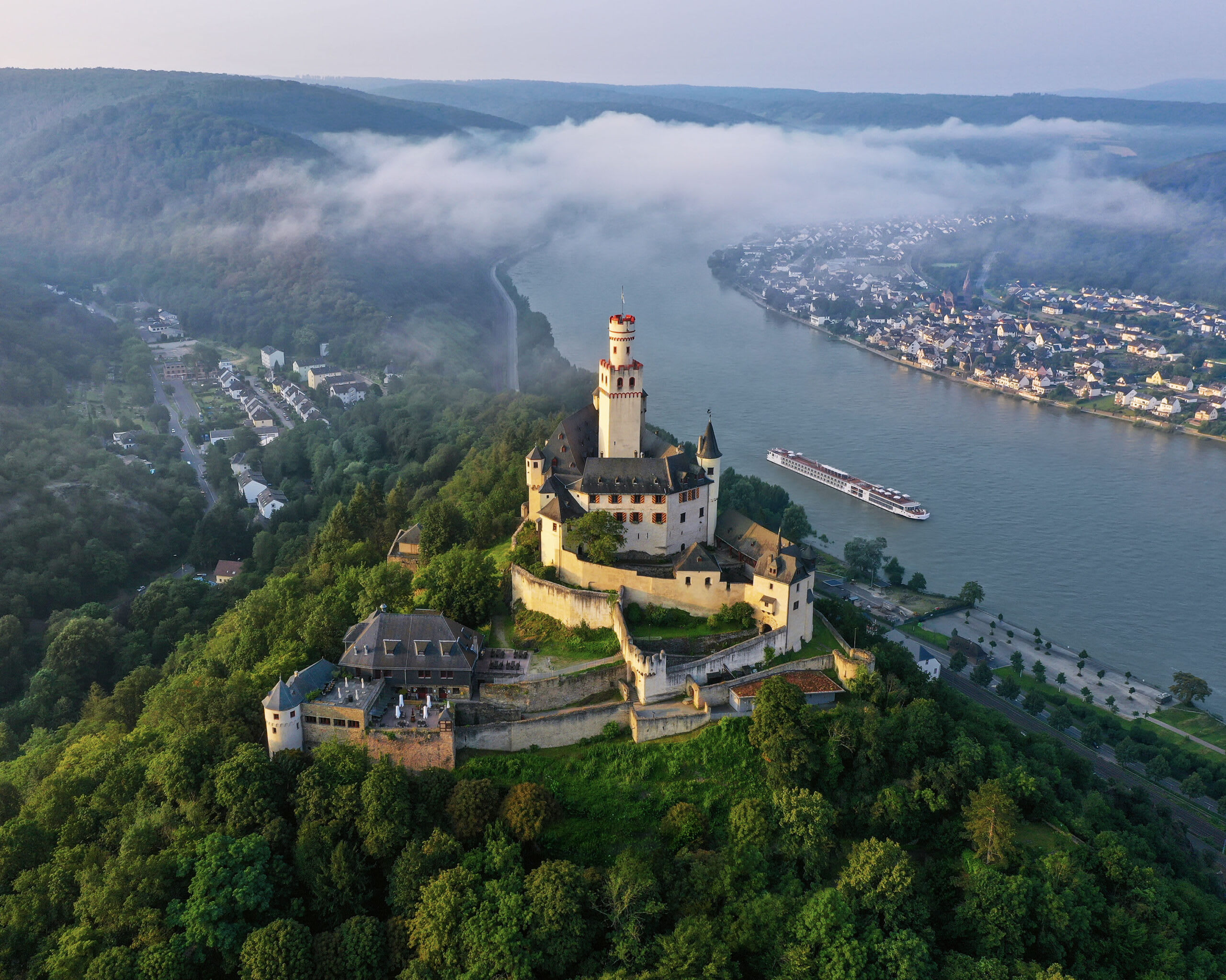 Marksburg Castle on the Rhine River A picturesque medieval castle perched on a forested hilltop overlooking the Rhine River, with