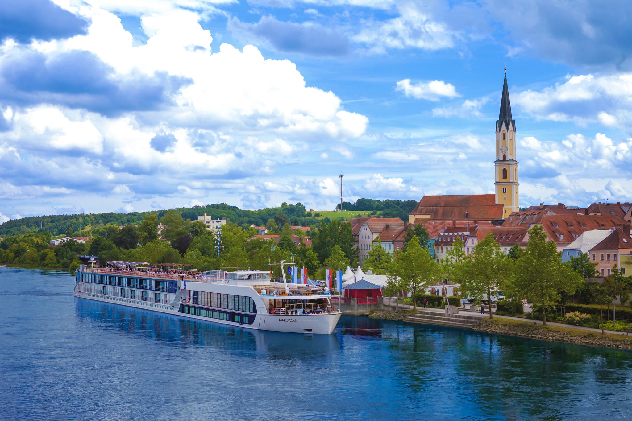 A modern river cruise ship docked alongside a picturesque European town with a tall church spire