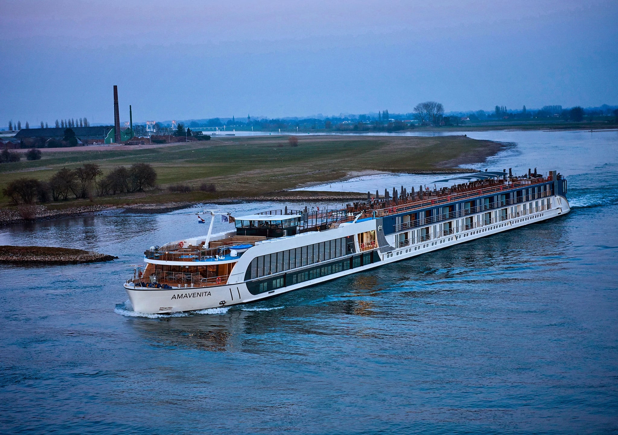 A modern river cruise ship named Amavenita sailing along a tranquil river with grassy banks