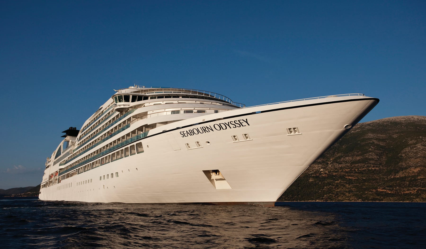 Seabourn Odyssey luxury cruise ship anchored in clear blue waters near rocky coastline