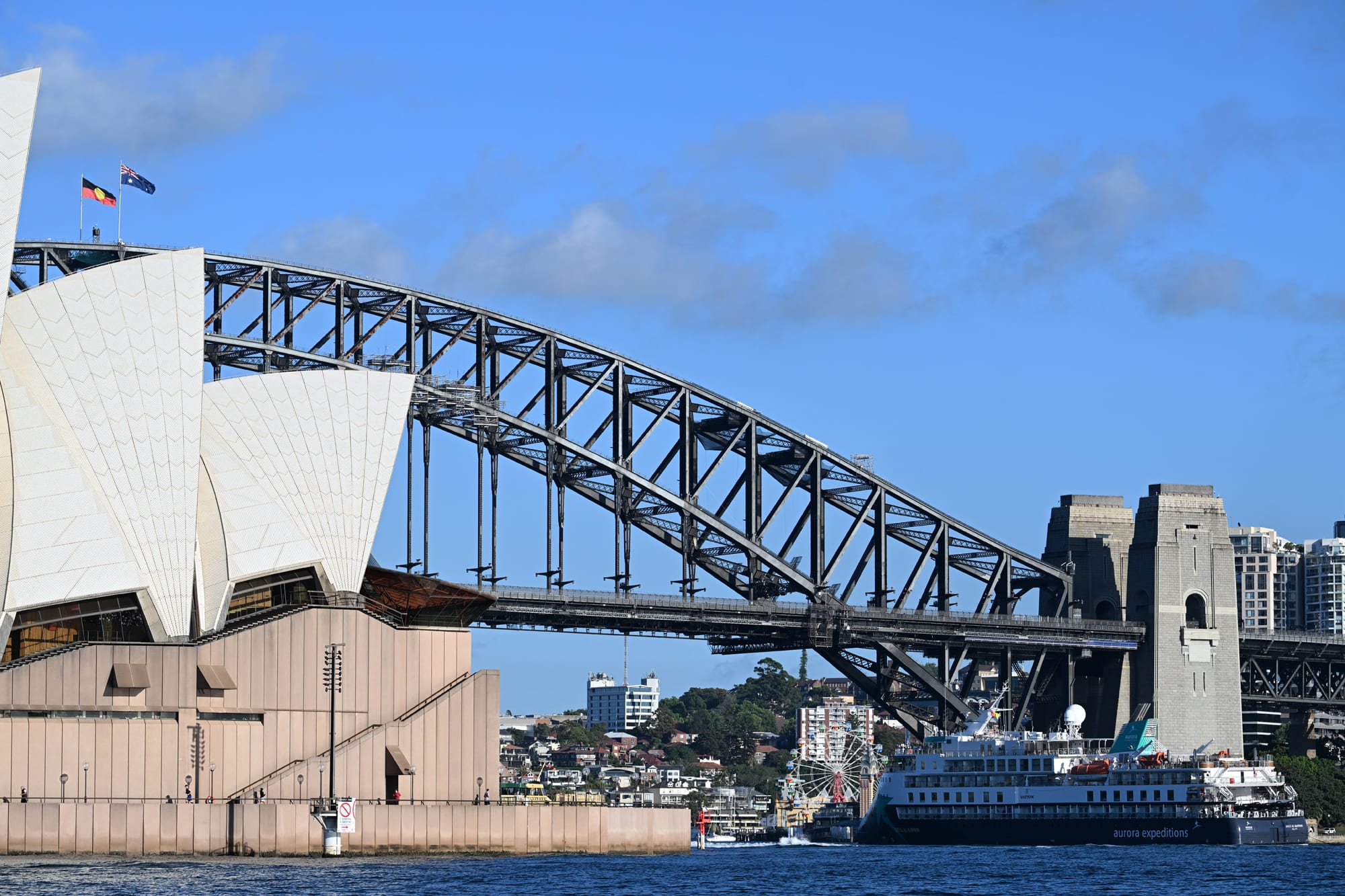 A panoramic view of Sydney Harbour featuring the Sydney Opera House and the Sydney Harbour Bridge