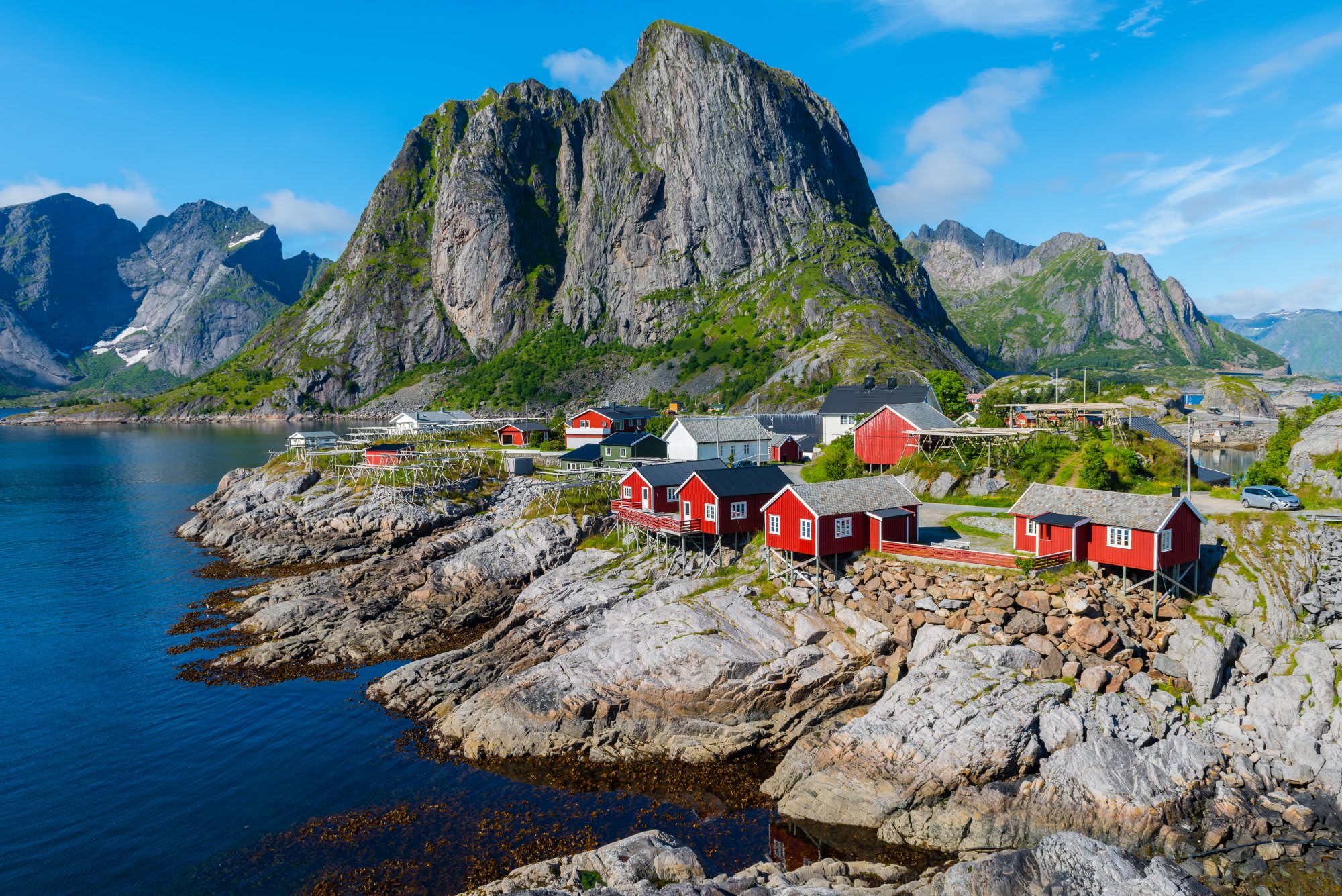shutterstock_756604909 Scenic Norwegian fjord with steep green mountainsides, a small village nestled at the water's edge, and a cruise ship sailing through the calm deep blue waters.
