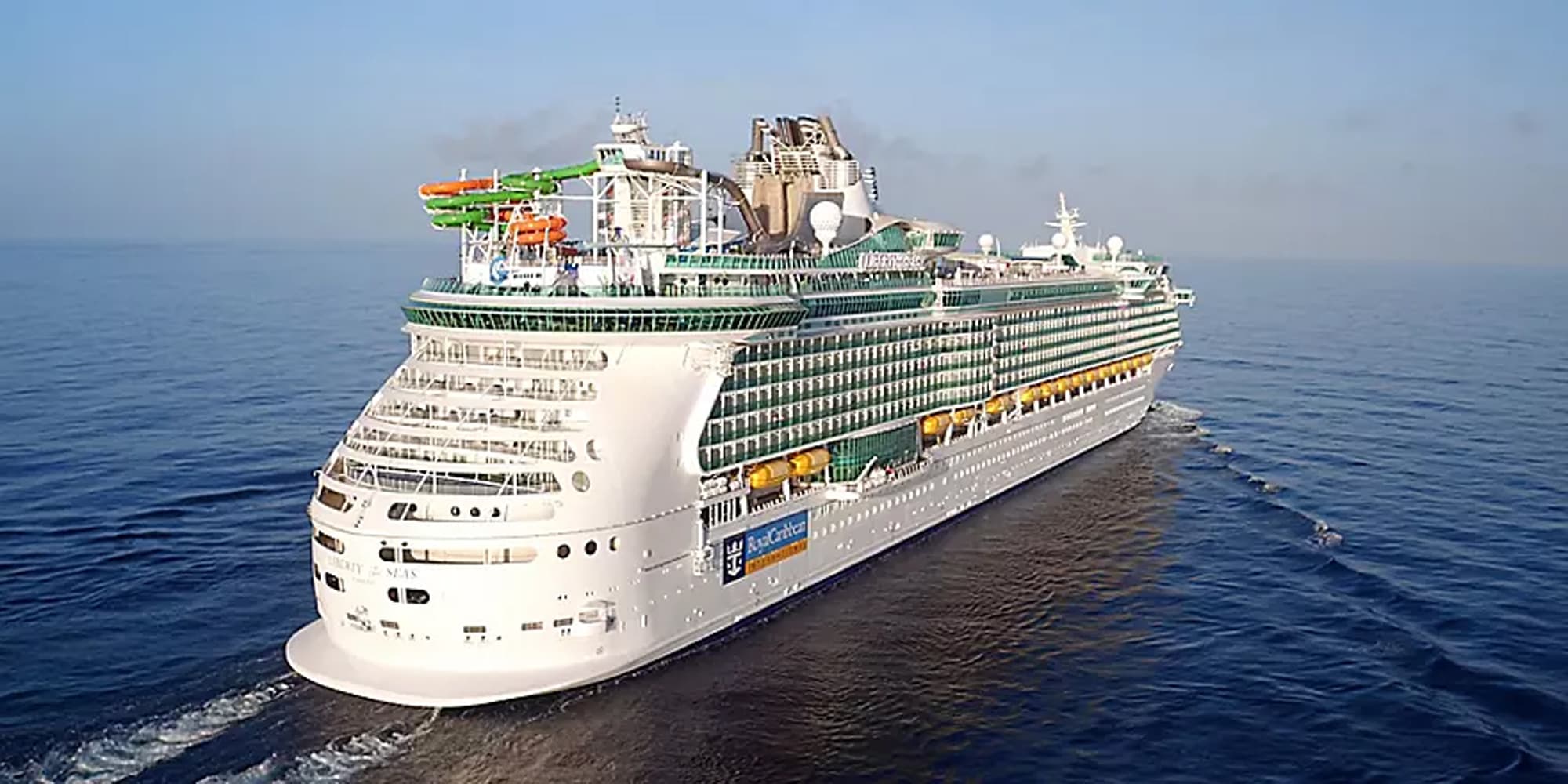 A large modern cruise ship photographed from an aerial perspective sailing on calm blue ocean
