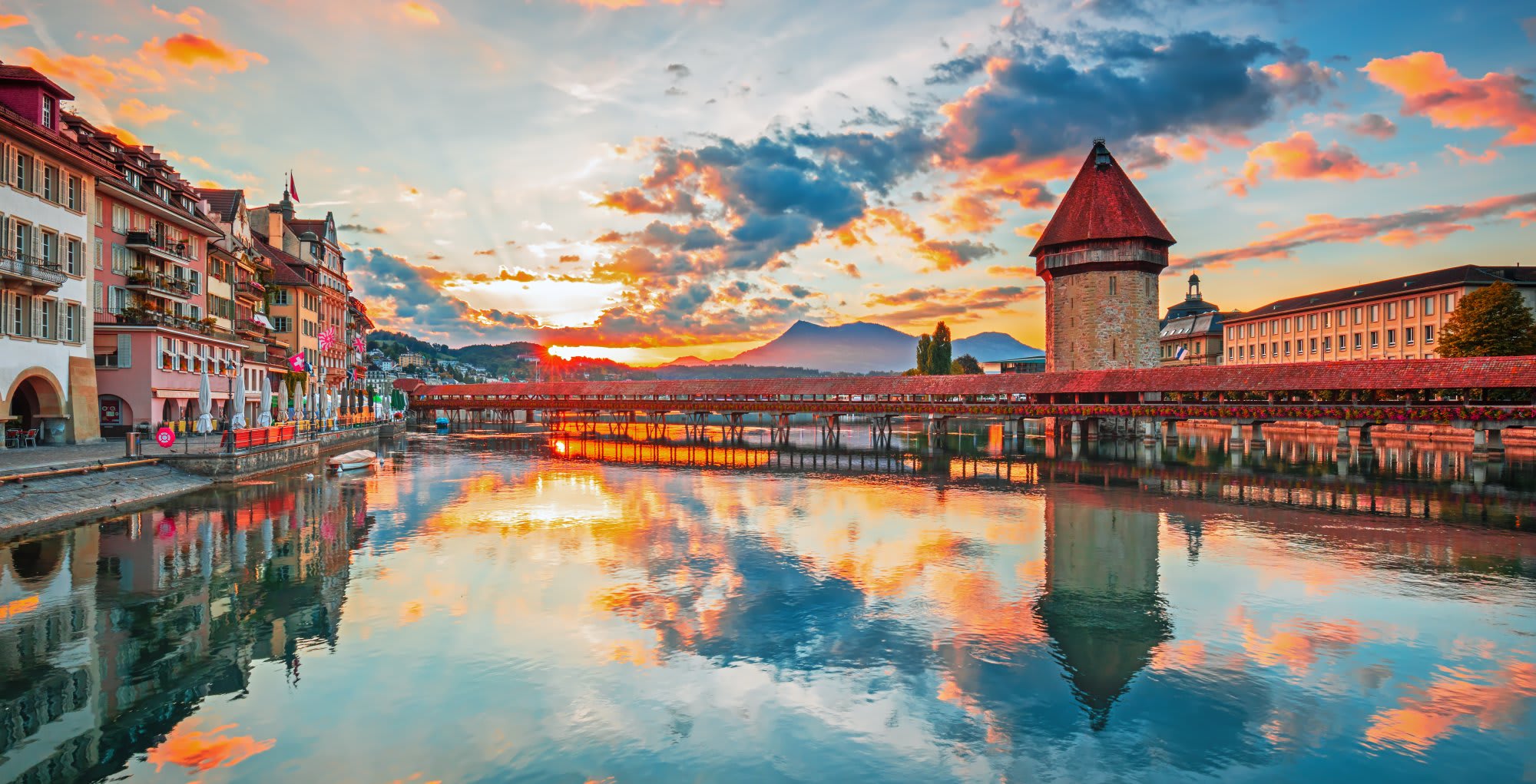 Lucerne Old Town Sunset with Chapel Bridge A stunning sunset view of Lucerne, Switzerland, featuring the iconic wooden Chapel Bridge with colorful medieval buildings reflected in the calm waters of Lake Lucerne.