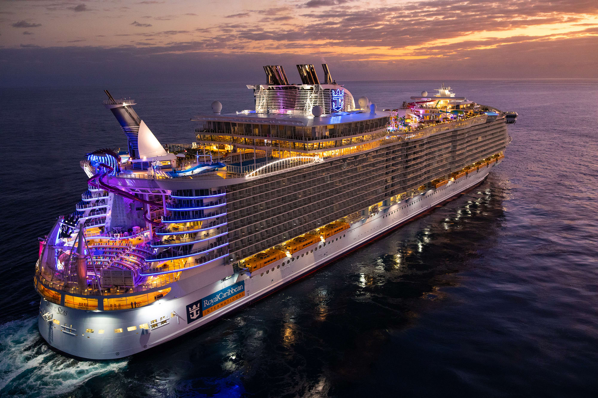 A massive modern cruise ship from Royal Caribbean illuminated at twilight, anchored in calm ocean