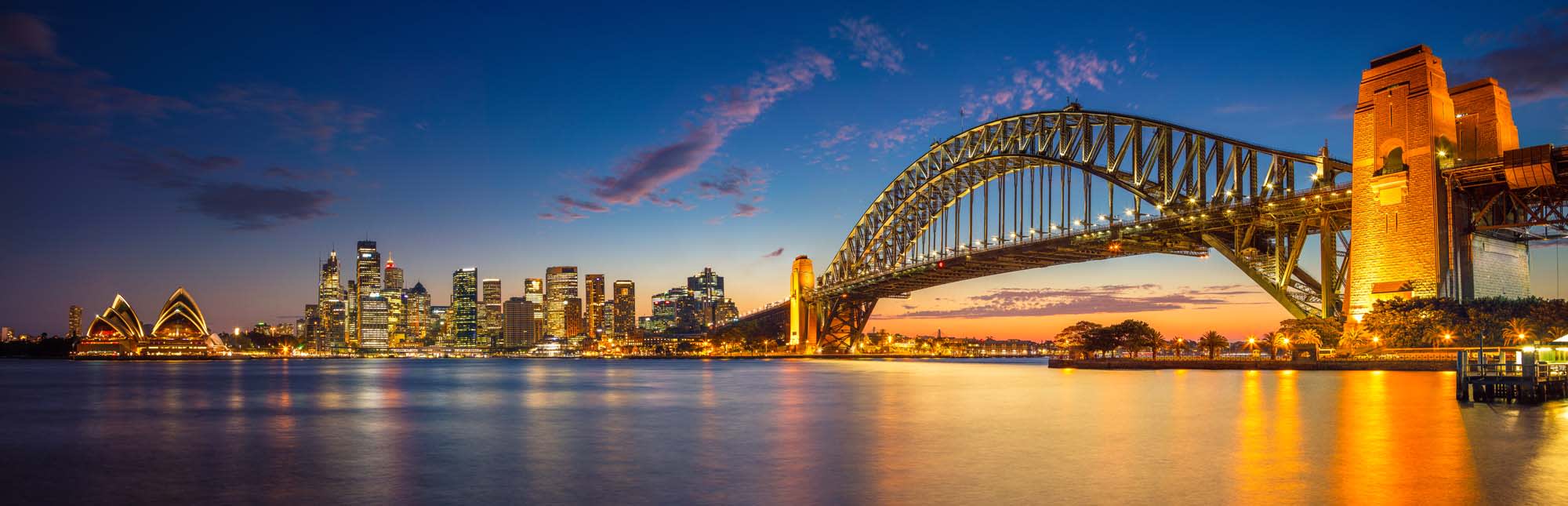 Sailing Ship in Milford Sound Fjord A stunning panoramic view of Sydney, Australia during the blue hour twilight, featuring the iconic Sydney Harbour Bridge illuminated in golden light, the distinctive Sydney Opera House on the left, and the glittering skyline reflected in the calm harbor waters.