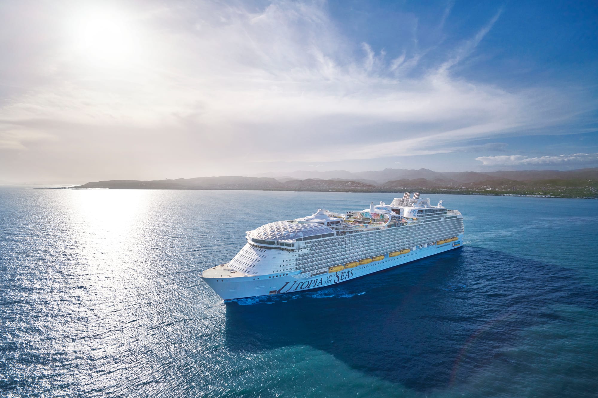 A large modern cruise ship anchored in bright blue tropical waters with a volcanic island coastline