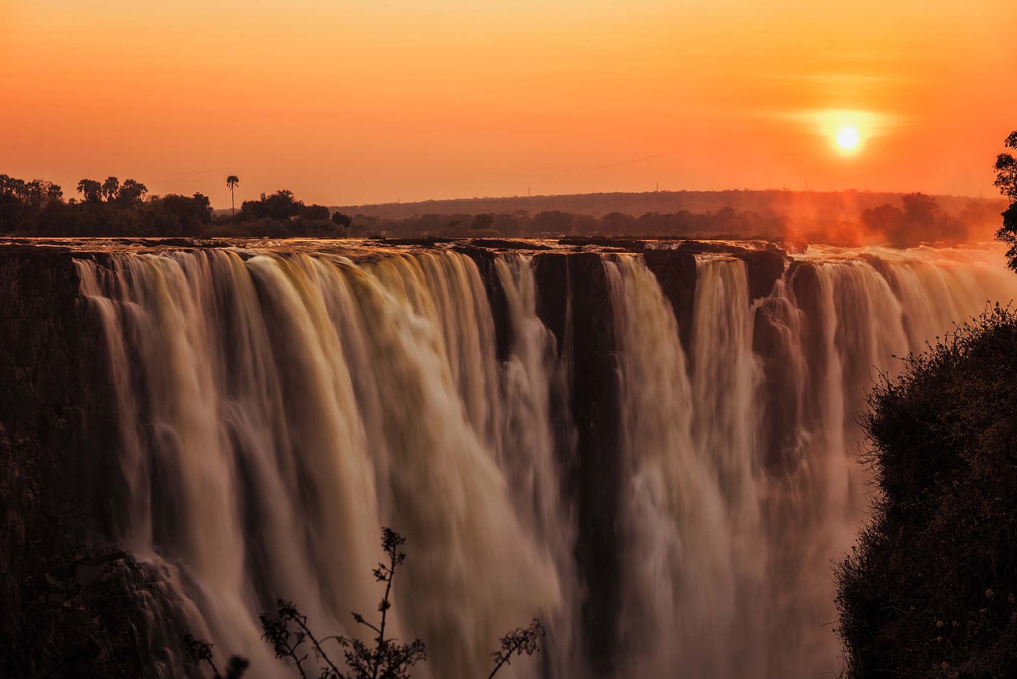 A breathtaking view of Victoria Falls at sunrise or sunset, with massive cascading waterfalls