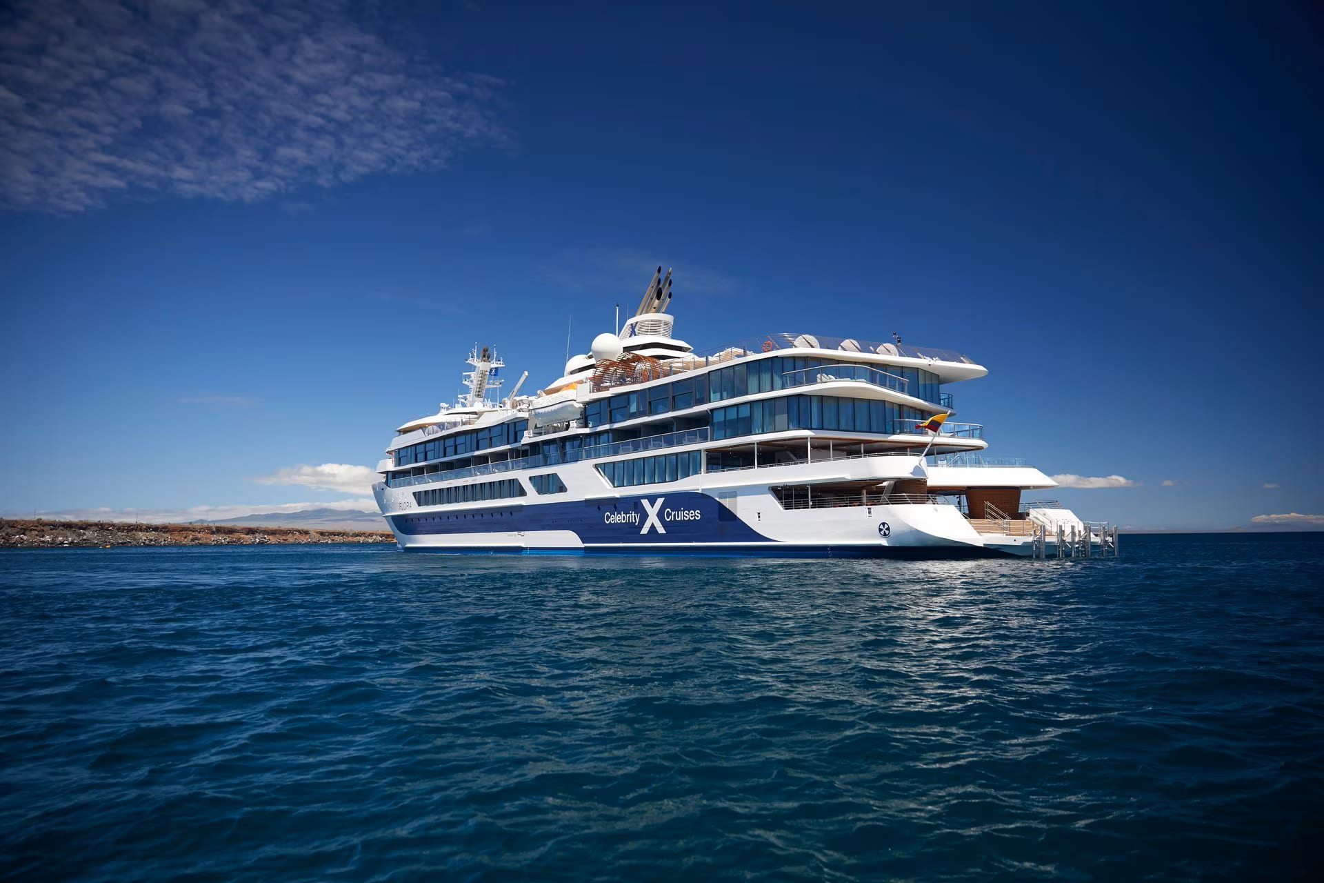 Celebrity Solstice cruising through crystal-clear tropical waters near a mountainous island coastline