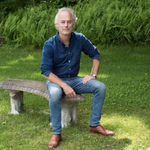 Photo of Amor Towles sitting on a stone bench in a green garden