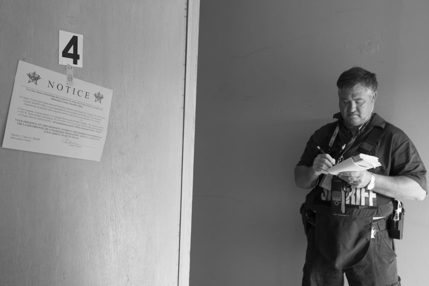 Sheriff writing in a notebook with eviction notice hanging in foreground.