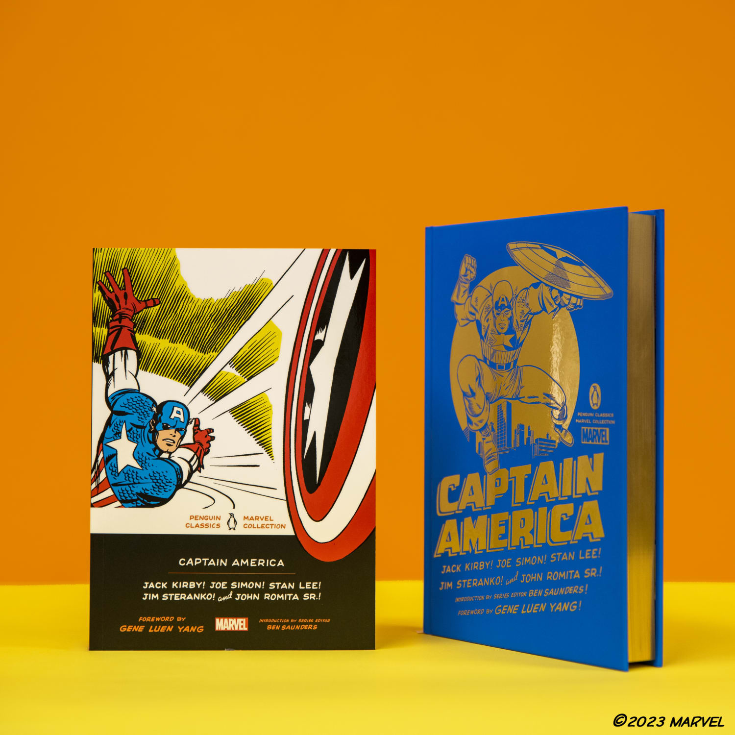 Captain America hardcover and paperback editions standing up against orange background