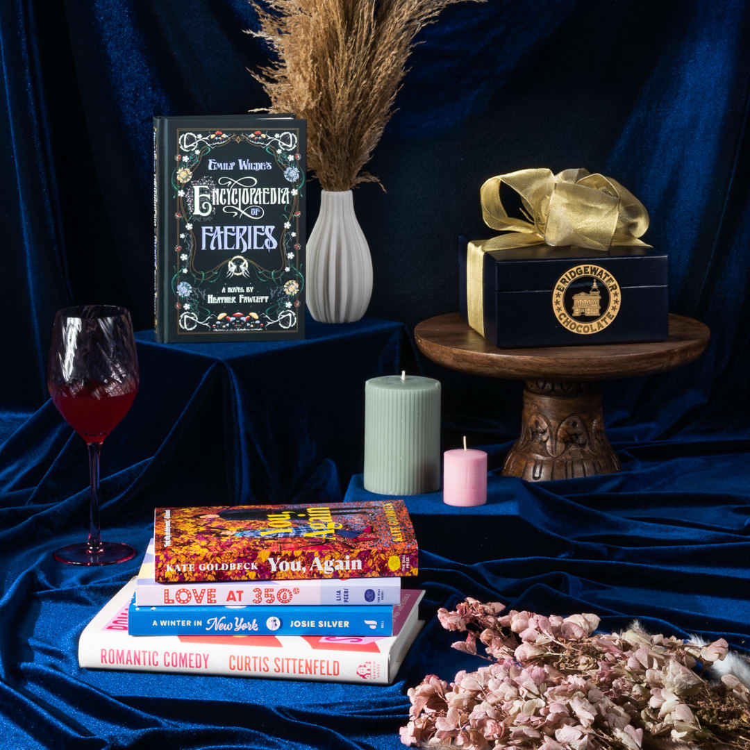 lifestyle image of blue velvet featuring books, chocolates from Bridgewater Chocolates, and dried flowers from Idlewild Floral.