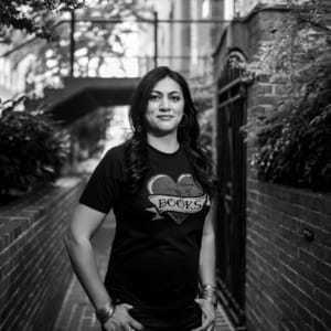 B&W photo of Sabaa Tahir, a Pakistani-American woman with long black hair wearing a black shirt that says "BOOKS" in a heart.