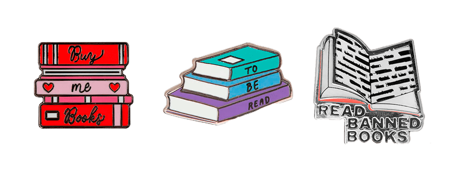 Three enamel pins pictured: one is a red and pink book stack with hearts on the spine that says, "Buy me Books;" the next one is a blue and purple stack of books that says "To Be Read" on the spines, and the third is an open book with the text blacked out that says "Read Banned Books" below it.