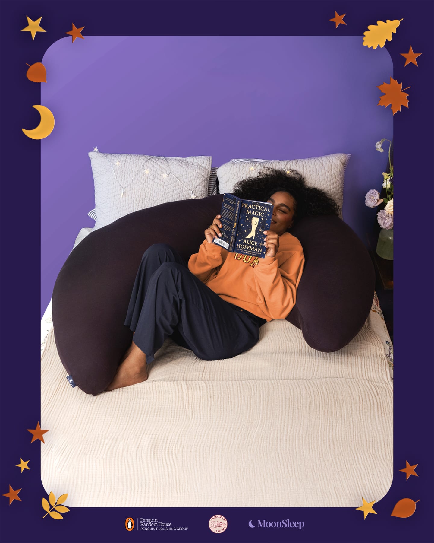 A girl with dark brown skin and curly hair lounges against a purple crescent shaped pillow on a bed with a light tan bedspread. She's reading Practical Magic by Alice Hoffman
