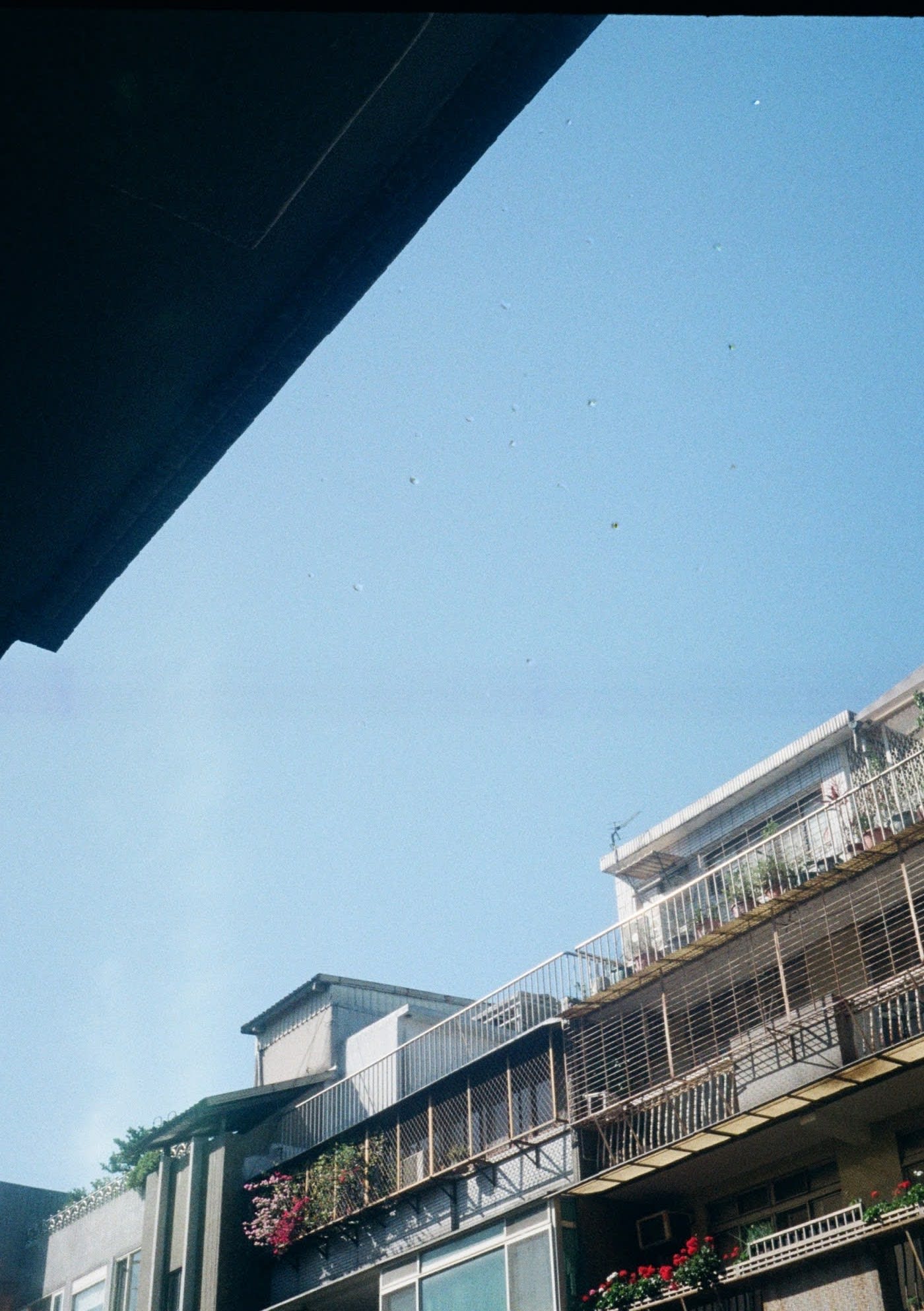 A photo looking up at the blue sky, with the upper floor balaconies of an apartment building visible in the lower half of the shot.