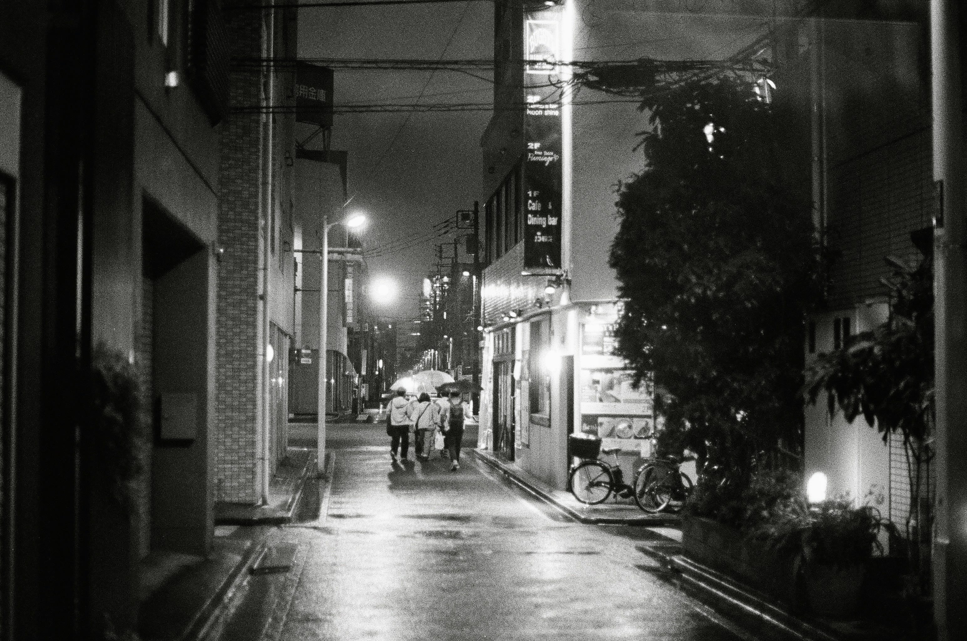 A family huddle under and umbrella running to find shelter in a sudden nightime downpour.