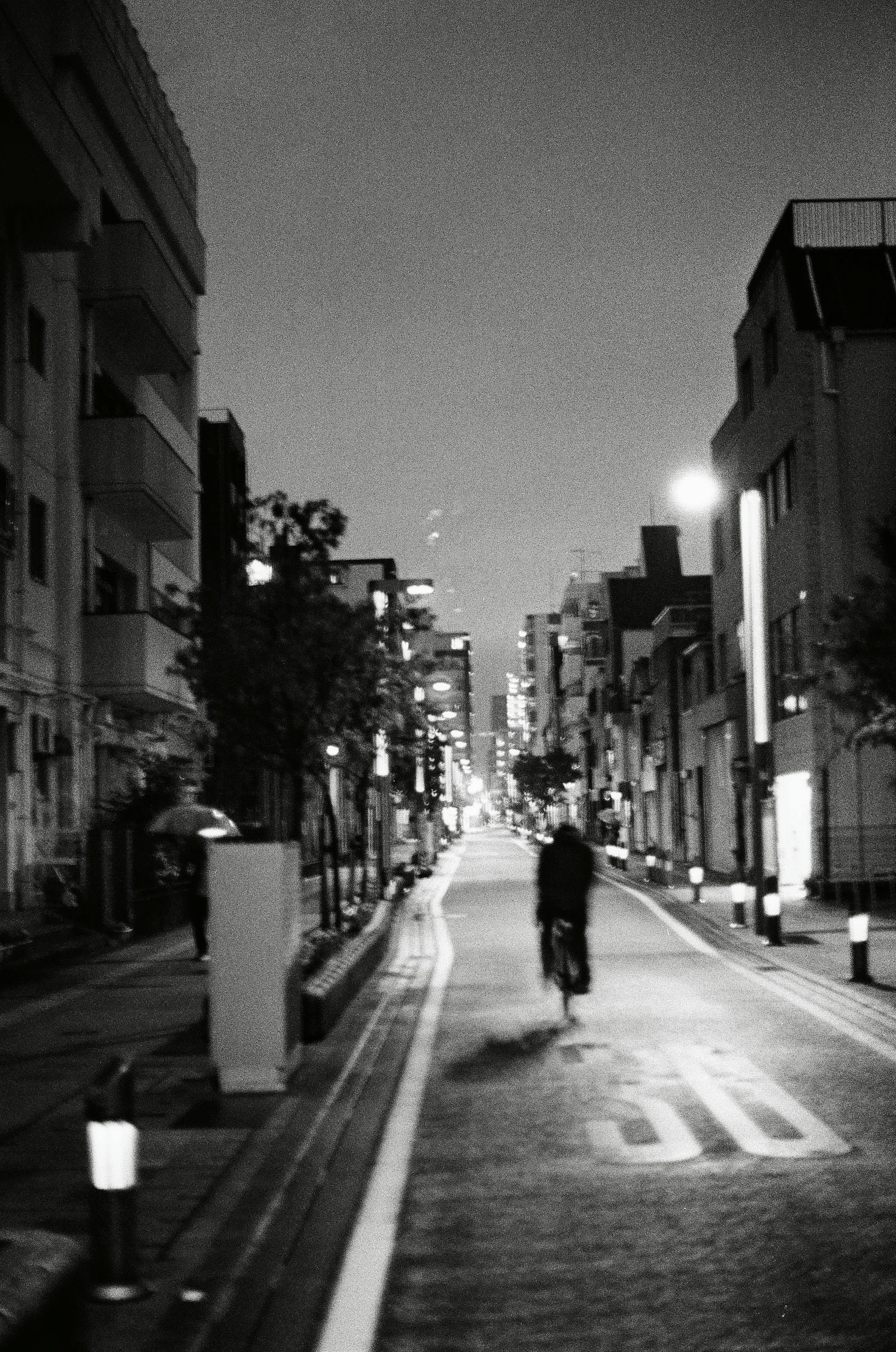 A blurry image shows a man in black riding a cycle in the middle of a narrow road at night.