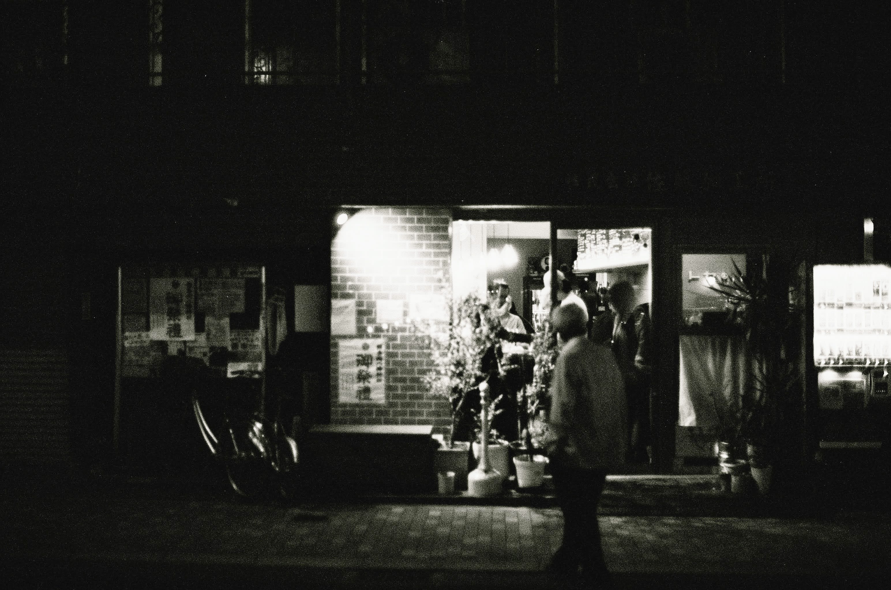 A man stands outside a lively bar looking in at the people enjoying themselves inside.