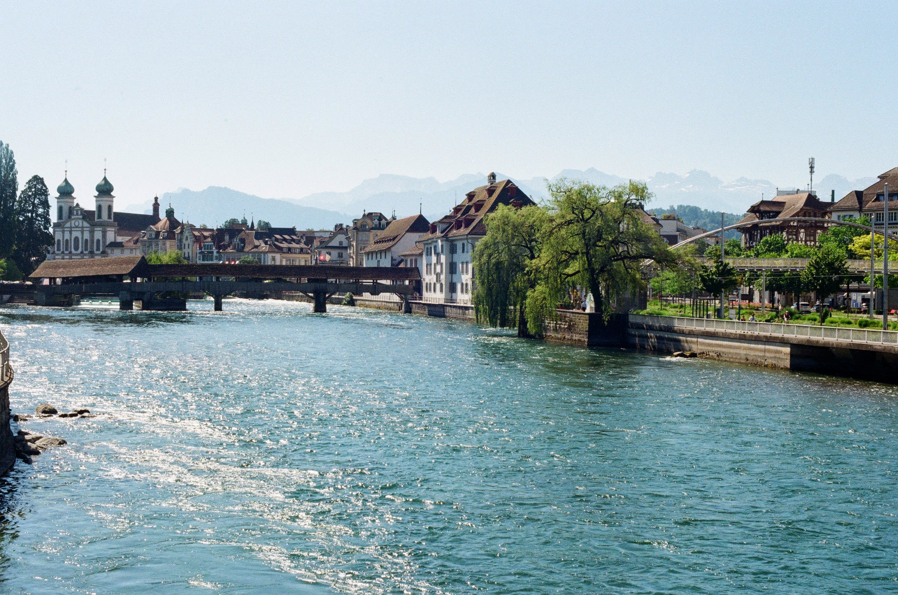 Looking down a fast flowing river towards the old town of Lucerne. Mountains rise above the city in the background.